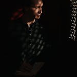 A priest sits in a dim confessional holding a Bible, reflecting faith and spirituality.