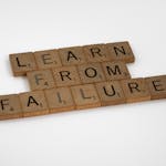 Wooden Scrabble tiles spelling 'Learn from Failure' on a white background, promoting resilience.